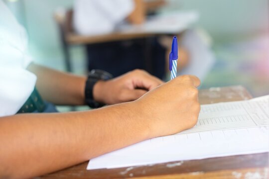 Close-up of Student Hand Writing on Exam Paper with Pen
High School Student Taking Standardized Test with Concentration on Wooden Desk