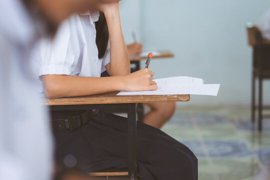 Stressed Female Student Holding Pen Writing Final Exam Paper in Classroom
