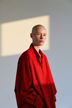 Studio portrait of bald model in oversized red top with rectangular sunlight patch and minimalist background for modern background