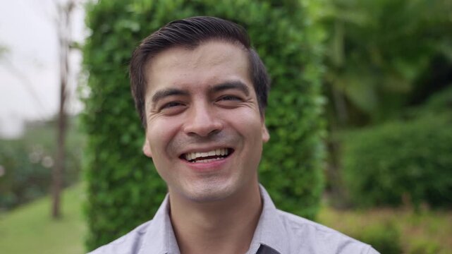 Close up of happy handsome Caucasian businessman in a shirt standing smiling while looking at the camera outdoors with cheerful while relaxing in the garden at a public park. 