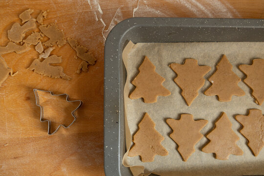 Christmas tree-shaped cookie cutter and gingerbread cookies on a baking sheet 