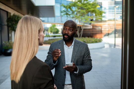 Businessman explaining to colleague outside office with smartphone