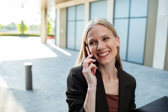 Smiling businesswoman talking on smartphone outside office building