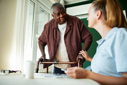 Caregiver assisting senior man standing with walker at home