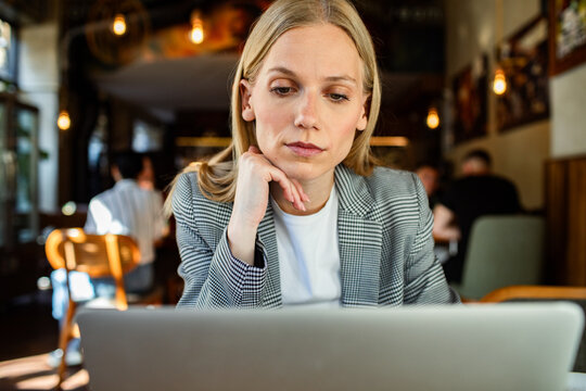 Professional woman resting chin while looking at a laptop in a cafe