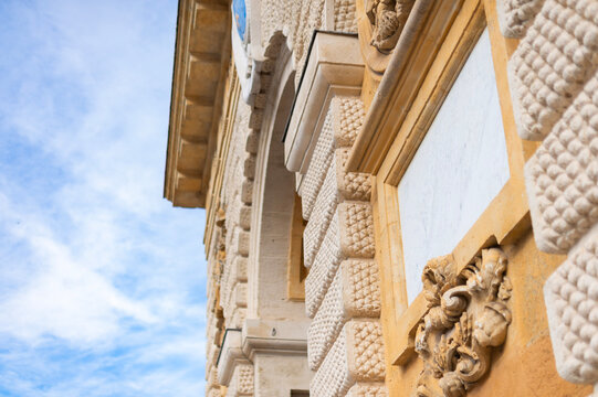 Intricate stone carvings and rusticated masonry decorate a historic facade in Montpellier, France. Low-angle architectural details frame an archway against a bright blue sky.