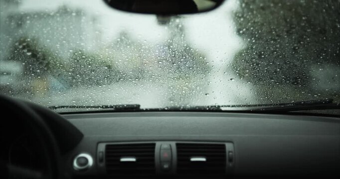 Raindrops on car windshield with oncoming vehicle headlights creating bokeh blur in background on rainy day