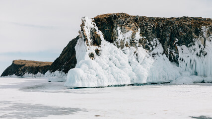 Majestic rocky cliff covered with thick snow and frozen ice splashes sits on the vast winter surface of Lake Baikal in Irkutsk Oblast, offering an arctic wilderness landscape view © TravelFlow