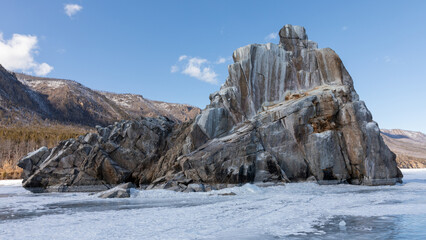 Majestic rocky cliff rises above the frozen snow covered surface of Peschanaya Bay on Lake Baikal in Irkutsk Oblast, Russia under a clear blue sky during calm bright winter season © TravelFlow