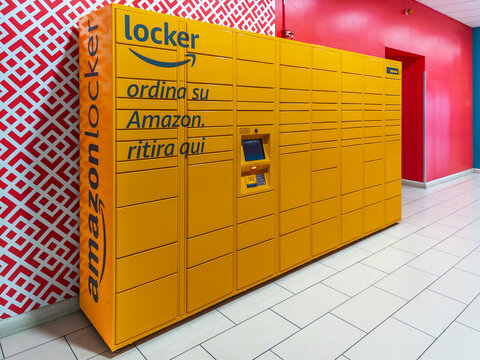 Italy - October 9, 2026: large yellow automated Amazon Locker station located inside italian commercial building with modern red and geometric patterned walls, providing self-service package pickup