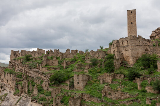 Scenic view of the ancient defensive stone watchtower and historic fortress ruins of Kahib village situated on a green mountain slope in Dagestan, Russia under a cloudy sky