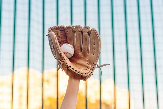 Baseball glove caught ball against stadium netting and blurred blue yellow autumn colors of nature.