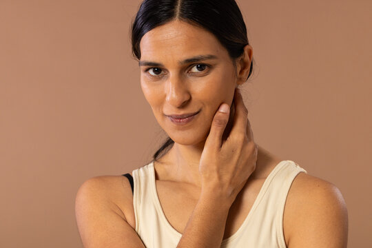 Indian woman posing in studio, touching neck, wearing cream sleeveless top with black strap