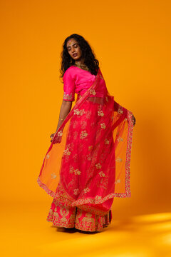 Indian adult woman posing in fuchsia outfit holding sheer embroidered dupatta on orange backdrop
