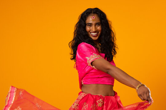 Indian woman twirling in studio wearing pink lehenga, gold maang tikka and bangles smiling