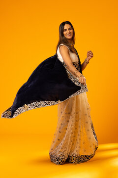Indian woman twirling in studio wearing navy dupatta and cream gold embroidered skirt with bangles