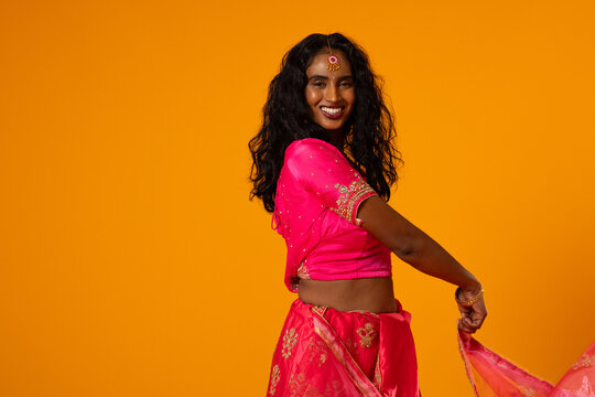 Woman posing in bright studio holding flowing pink drape wearing gold embroidered sari and bindi