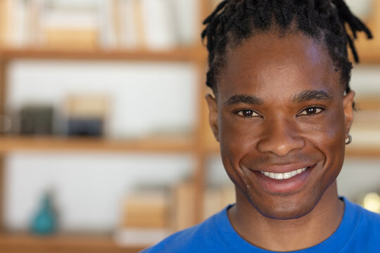 African man smiling and looking at viewer in home study wearing blue T-shirt with bookshelf