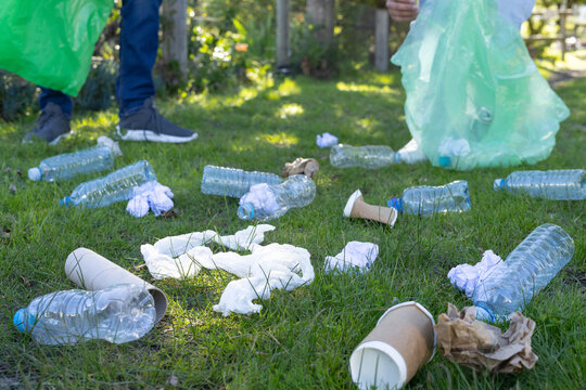 Two volunteers picking up bottles and cups on park grass with green bags wearing gloves