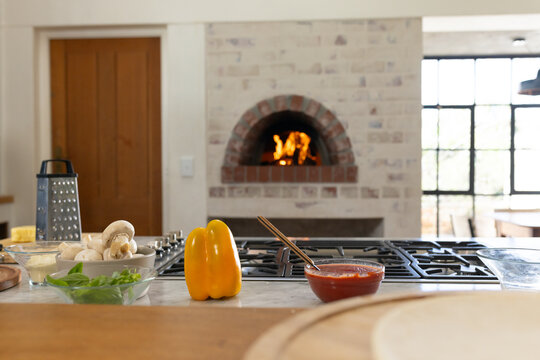 Yellow bell pepper is sitting on kitchen countertop near bowls, grater, board, oven flame, window