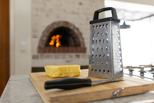 Stainless steel four sided box grater standing on wood board by oven flame, with butter