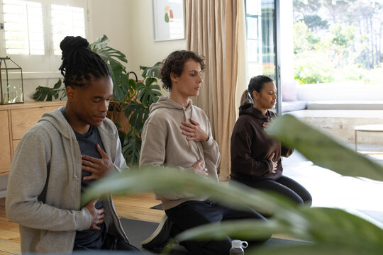 African American peers kneeling and practicing breathing on yoga mats with water bottle at home