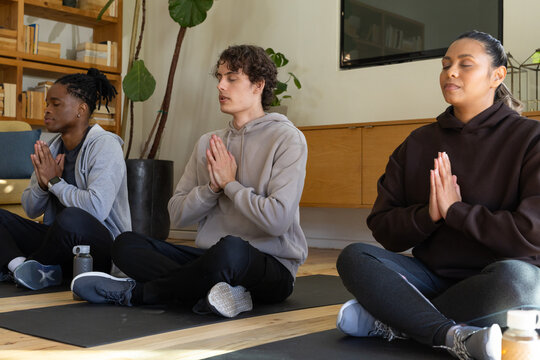 Diverse group meditating cross-legged on three yoga mats in studio with water bottle nearby