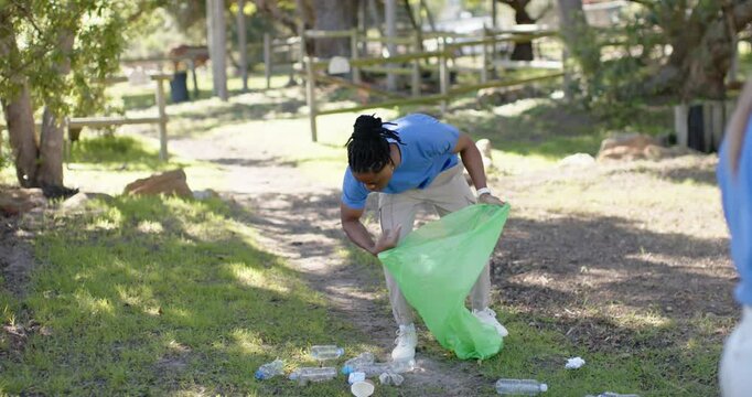 African American man wearing blue shirt placing bottles in green bag at park after spotting litter