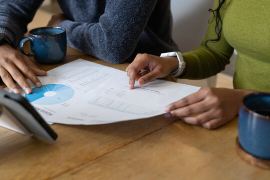 Indian man and Asian woman pointing at pie chart at table with blue mugs and tablet