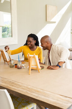 African American couple painting on small tabletop easels at large wooden table with paintbrushes