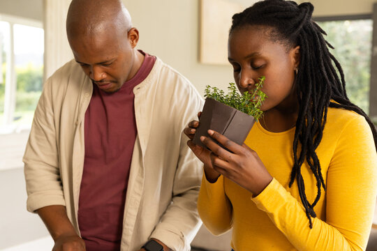 African American couple cooking at counter, woman in mustard top smelling herb pot