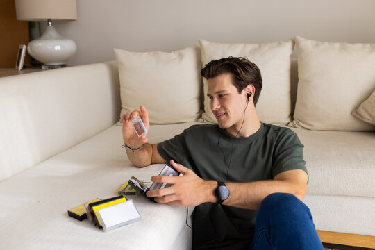 Man in dark green tee, jeans sitting on floor at home, holding cassette player and tape