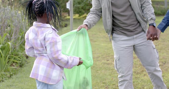 African American family spotting litter, holding green trash bag, cleaning park and highfiving