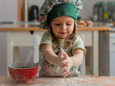 Cute toddler smiling girl claps hands covered in white flour over wooden table. Christmas home baking process perfect for cooking class or family activity themes