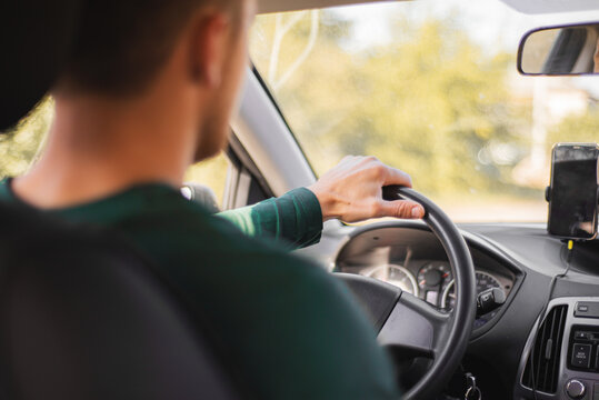 Man Driving Car With Smartphone Mounted on Dashboard. Over the shoulder view of a man holding the steering wheel while driving, with a smartphone mounted on the dashboard and warm sunlight illuminatin