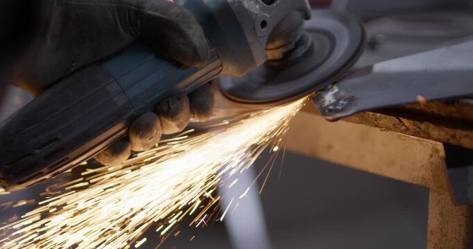 Worker grinding steel edge angle grinder, bright sparks workshop metal shaping