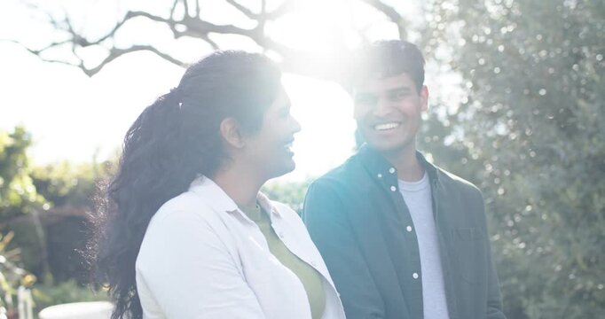 Indian man and Asian woman holding seedling, cupping soil to plant, laughing in garden