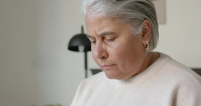 Senior woman reading offscreen document lifting gaze seeing lamp and pondering in home room