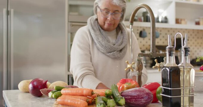 African American woman spotting vegetables rinsing and rubbing produce at sink, preparing dinner