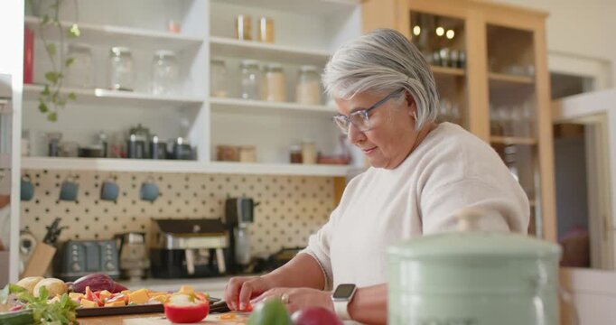 Senior African woman reaching for cutting board, slicing tomatoes and peppers for meal in kitchen