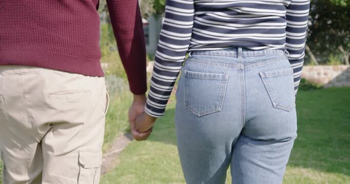 Camera starting follow is tracking couple walking hand in hand toward house on sunlit garden path