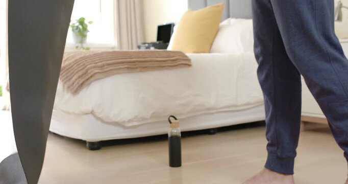 Man is adjusting grip, unrolling dark-gray mat and stepping onto it on bedroom floor for workout