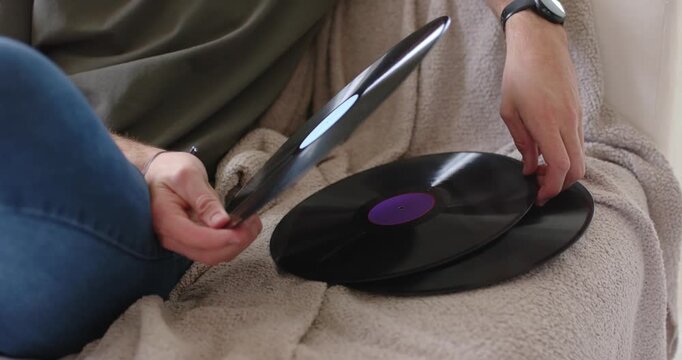 Seated man is reaching for stacked vinyl on sofa, sliding record, inserting card, checking labels