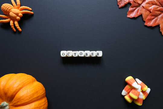 October spelled with letter tiles on black background with pumpkin, candy corn, toy spider and autumn leaves for a seasonal Halloween concept.