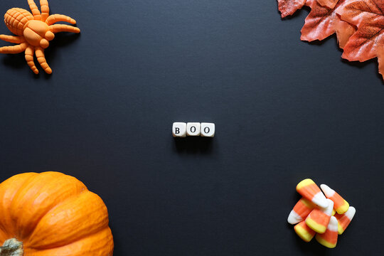 Boo spelled with letter tiles on black background with pumpkin, candy corn, toy spider and autumn leaves for a Halloween concept.