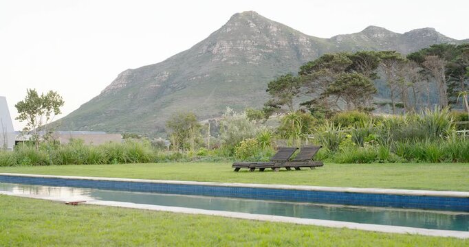 Camera is panning right, revealing two dark wood loungers beside narrow pool, showing shed and peak