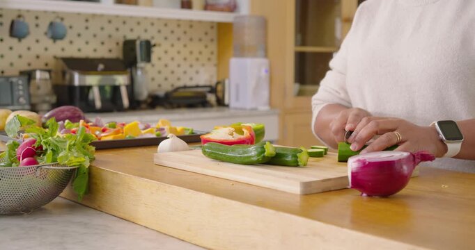 Hands are placing green cucumber on cutting board and are slicing even rounds for salad prep