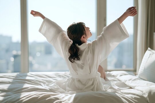 朝日に照らされベッドで伸びをする若い日本人女性の快適な時間