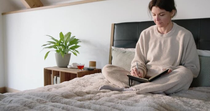 Woman writing in black notebook on lap stand on bed, clearing mind, closing journal and meditating
