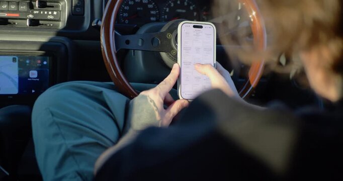 Man using a smartphone to write notes, check work emails, or send text messages while sitting inside a car. Driver reads news and records information on a mobile phone inside a parked vehicle.